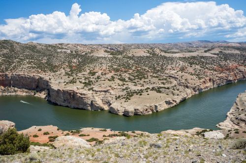 A winding river flows through a rocky landscape under a blue sky with fluffy clouds.