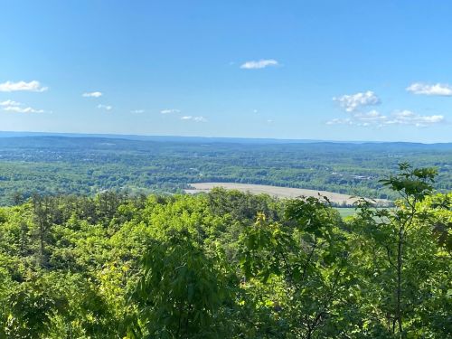 A panoramic view of lush green hills and valleys under a clear blue sky with scattered clouds.
