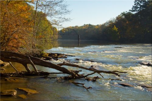 A serene river scene with flowing water, rocky banks, and autumn foliage under a clear blue sky.
