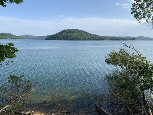 A serene lake scene with gentle waves, surrounded by green hills and trees under a clear blue sky.
