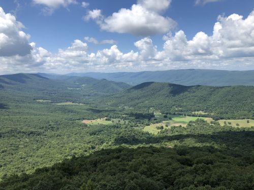 A panoramic view of lush green mountains and valleys under a blue sky with fluffy white clouds.