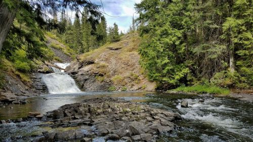 A serene landscape featuring a waterfall cascading into a rocky river, surrounded by lush green trees and hills.