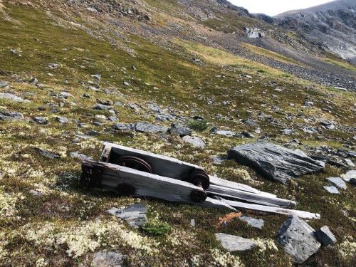 An old wooden cart with wheels rests on a rocky, grassy hillside under a clear sky.