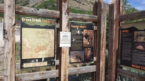 Signage at Grove Creek Trailhead displaying maps, wildlife information, and safety guidelines in a natural setting.