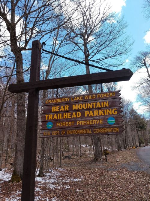 Sign for Bear Mountain Trailhead Parking in Cranberry Lake Wild Forest, surrounded by trees and a blue sky.