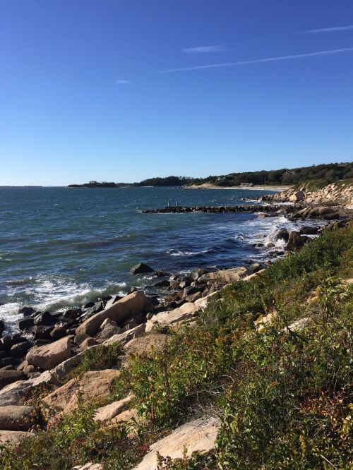 A scenic coastal view with rocky shores, gentle waves, and clear blue skies.