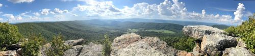 A panoramic view of lush green mountains and valleys under a bright blue sky with fluffy white clouds.