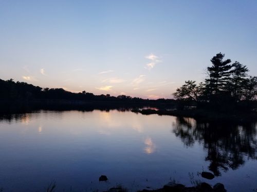 A serene lake at sunset, reflecting the sky and trees, with calm water and a peaceful atmosphere.