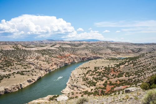 A winding river flows through a rugged landscape of hills and sparse vegetation under a blue sky with clouds.