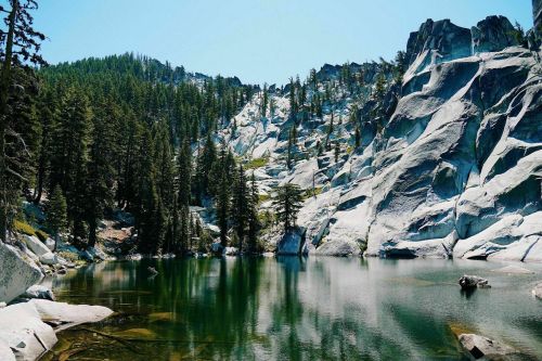 A serene lake surrounded by tall trees and rocky cliffs under a clear blue sky.