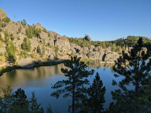 A serene lake surrounded by rocky cliffs and lush trees under a clear blue sky.