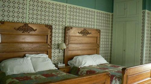 A cozy room with two wooden beds, floral quilts, and patterned wallpaper. A wardrobe is visible in the background.