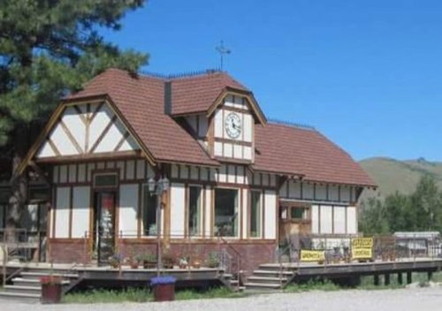 A charming, rustic building with a clock tower, surrounded by trees and a clear blue sky.