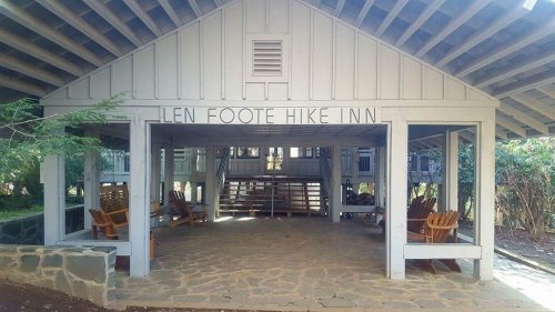 A wooden structure with a sign reading "Len Foote Hike Inn," featuring seating and surrounded by greenery.