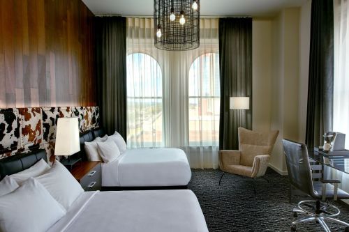 A stylish hotel room featuring two beds, large windows, modern decor, and a cozy seating area.