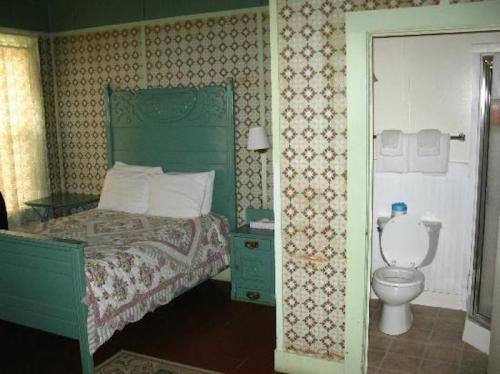 A cozy bedroom with a green bed frame, patterned wallpaper, and an adjoining bathroom with a toilet and shower.