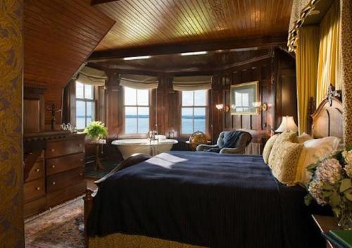 Cozy bedroom with wooden walls, large windows, a plush bed, and a vintage bathtub overlooking a scenic view.