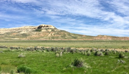A wide landscape featuring rolling hills, green grass, and a blue sky with scattered clouds.