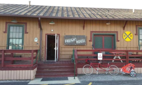 A rustic building with a sign reading "The Freight House," featuring a porch and a bicycle parked outside.
