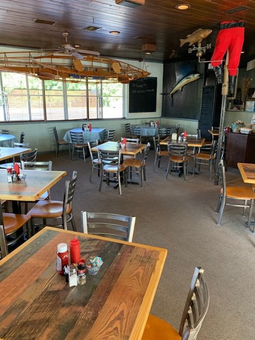 A cozy restaurant interior with wooden tables, metal chairs, and a fishing theme, featuring a large fish on the wall.