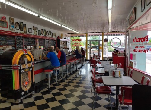 A retro diner interior with checkered floors, a jukebox, and patrons sitting at the counter enjoying their meals.