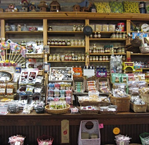 A colorful display of various candies, jars, and snacks arranged on wooden shelves in a charming store.