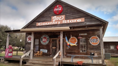 A rustic wooden country store with vintage signs, including Coca-Cola and Gulf, set in a rural landscape.
