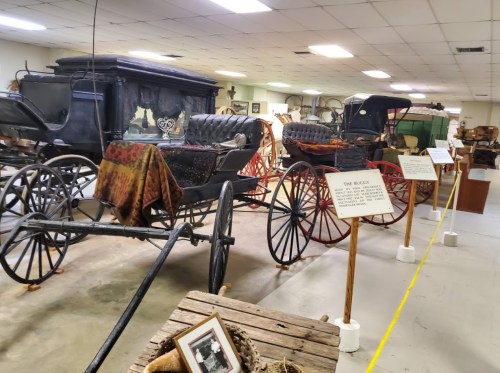 A display of vintage horse-drawn carriages in a museum, with informational signs and various artifacts.