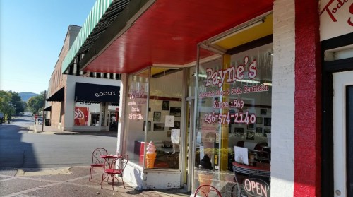 Exterior of Payne's Soda Shop and Ice Cream Fountain, featuring red accents and outdoor seating, in a quaint downtown area.