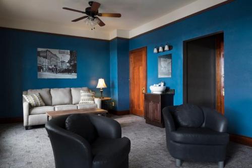 Cozy living room with blue walls, a sofa, two black chairs, a wooden table, and a lamp.