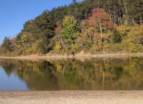 A serene lake reflects colorful autumn trees under a clear blue sky.