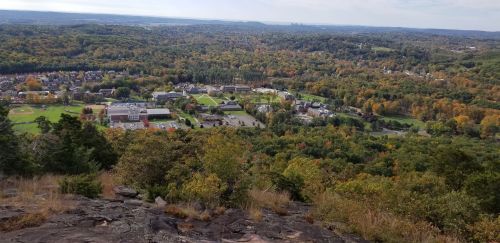 A panoramic view of a colorful autumn landscape with a town and fields nestled among trees from a rocky overlook.