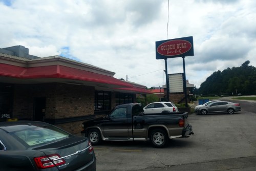 Exterior of Golden Rule Bar-B-Q restaurant with parked cars and a cloudy sky in the background.