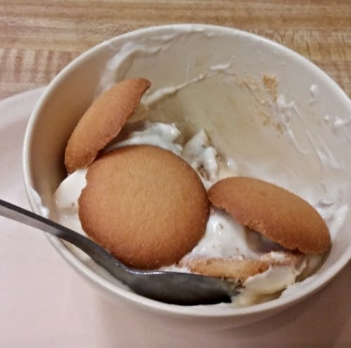 A bowl of ice cream with several vanilla wafers and a spoon, partially eaten.
