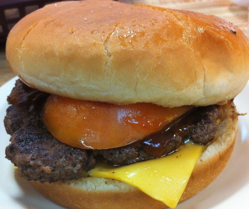 A close-up of a hamburger with a beef patty, melted cheese, a slice of tomato, and a soft bun.