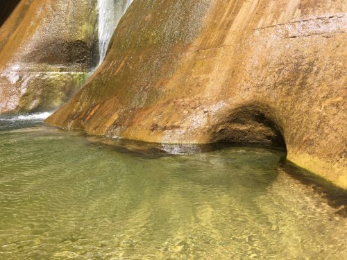 A serene water pool surrounded by smooth, weathered rock formations and a gentle waterfall in the background.