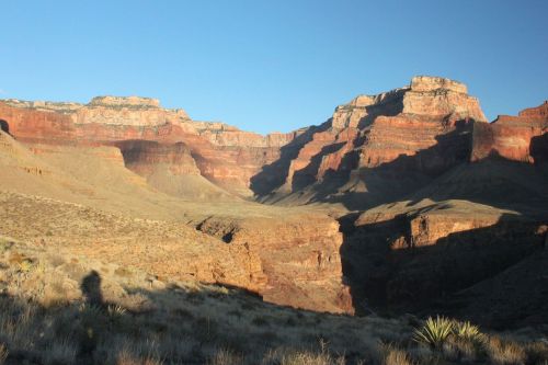 A scenic view of the Grand Canyon, showcasing layered red rock formations and a clear blue sky.