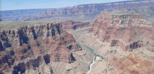 Aerial view of the Grand Canyon, showcasing layered red rock formations and the winding Colorado River below.