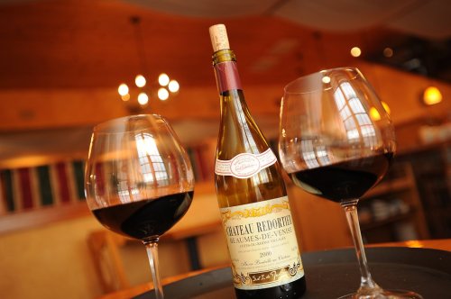 A bottle of Château Redortier wine with two filled glasses, set on a table in a warm, inviting restaurant.