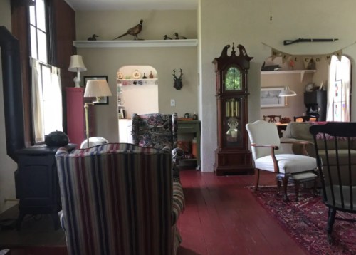 Cozy interior of a room with vintage furniture, a patterned chair, and decorative items on shelves and walls.