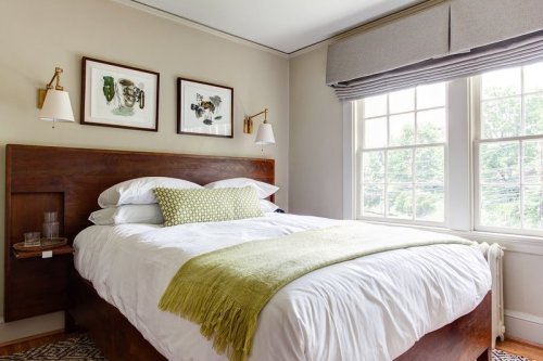 Cozy bedroom with a wooden bed, white bedding, green throw, and framed art on the walls, featuring a large window.