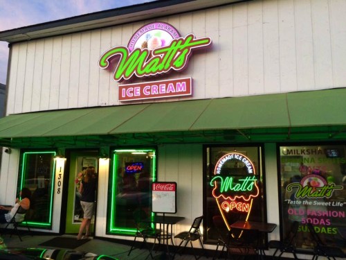 A brightly lit ice cream shop with neon signs, featuring outdoor seating and a welcoming entrance.