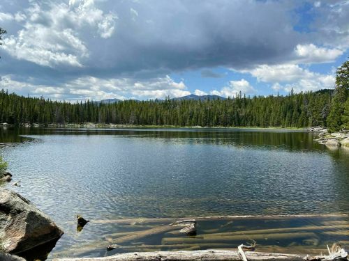 A serene lake surrounded by lush green trees and mountains under a partly cloudy sky.