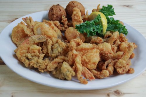 A plate of assorted fried seafood, including shrimp and hushpuppies, garnished with lemon and kale.