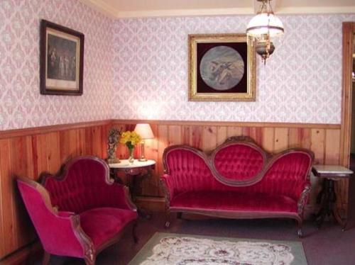 A vintage living room with red velvet furniture, floral decor, and a framed painting on patterned wallpaper.