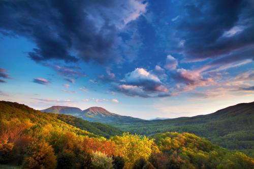 A vibrant landscape of mountains and colorful autumn foliage under a dramatic sky with clouds.