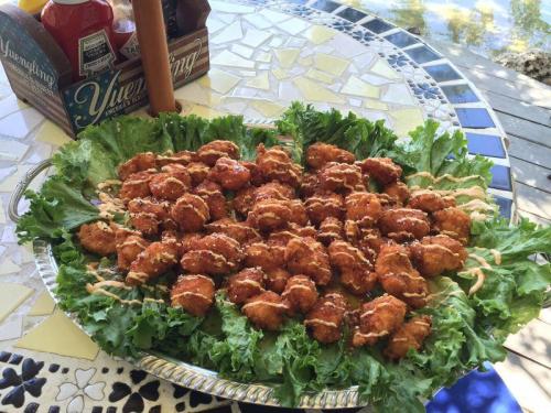 A large platter of golden-brown fried food on a bed of lettuce, drizzled with sauce, set outdoors.