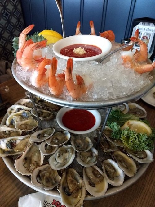 A seafood platter featuring shrimp, oysters on ice, and dipping sauces, garnished with lemon and lettuce.