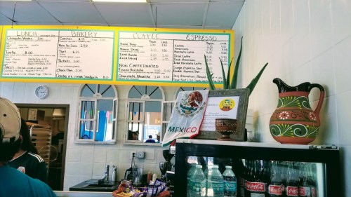 A colorful menu board at a café, listing lunch, bakery items, and coffee options, with a decorative pitcher and flag.