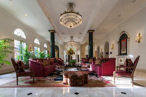 Elegant lobby with plush seating, a large chandelier, and decorative plants, featuring a rich color palette and ornate decor.